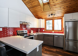 Kitchen renovation featuring two-toned white and warm grey cabinets, clean white countertops, stainless steel appliances, natural wood flooring, and red tile backsplash for a pop of colour.