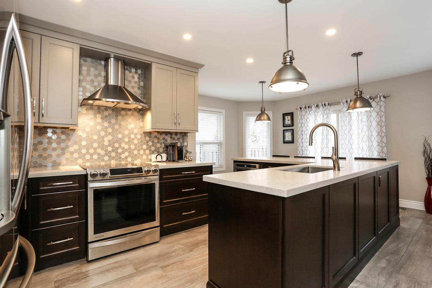 Kitchen design with large island with eating bar, warm grey and dark brown cabinets, stainless steel appliances, and stunning mosaic backsplash - total living concepts in barrie ontario