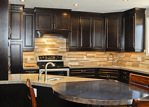 Warm kitchen design utilizing dark and light brown tones throughout including dark wood cabinets, hardwood floors, and backsplash, with stainles steel appliances and unique round steel eating bar - Total Living Concepts barrie ontario