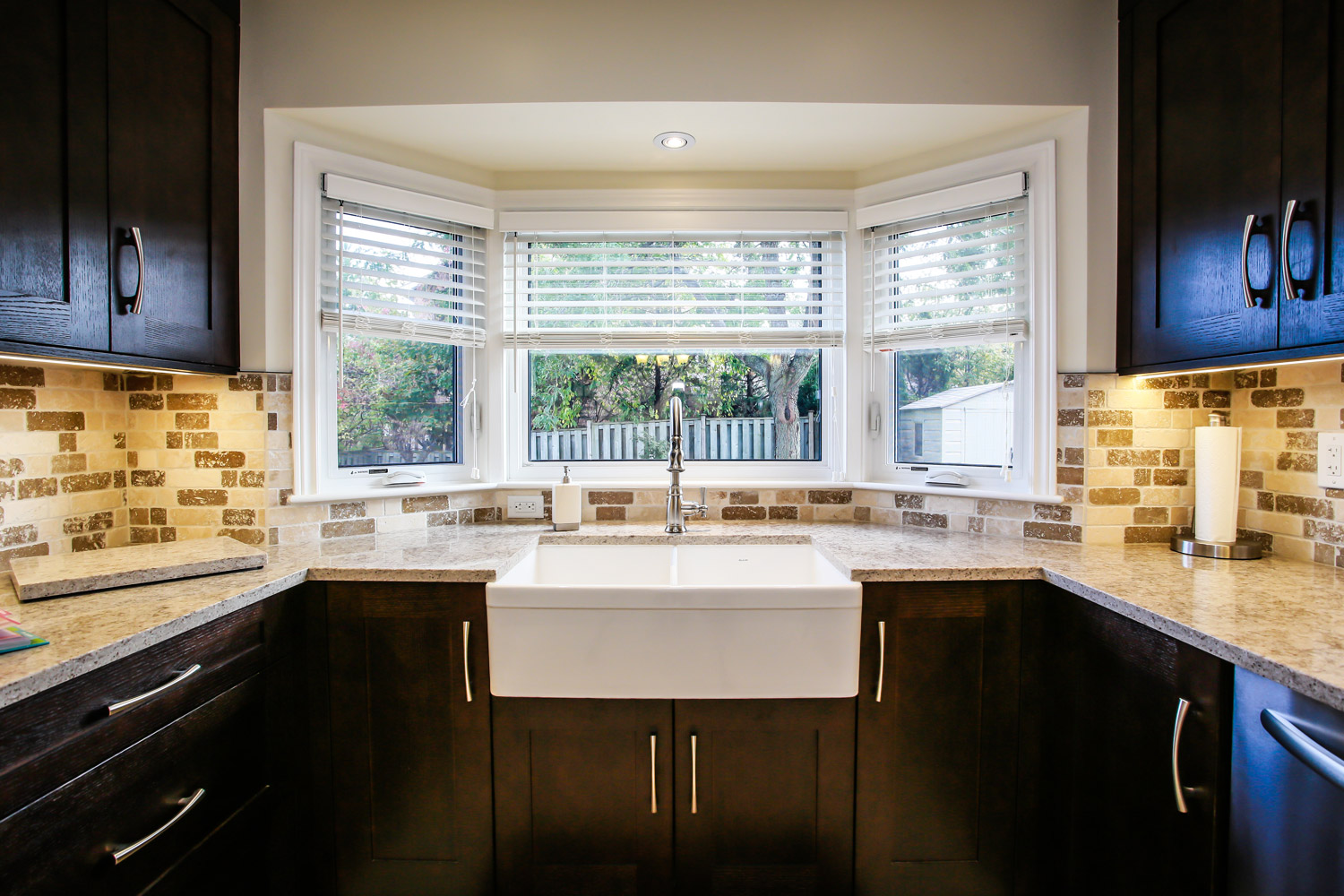 Transitional kitchen with dark wood cabinets, white farmhouse apron kitchen sink, earth tone backsplash