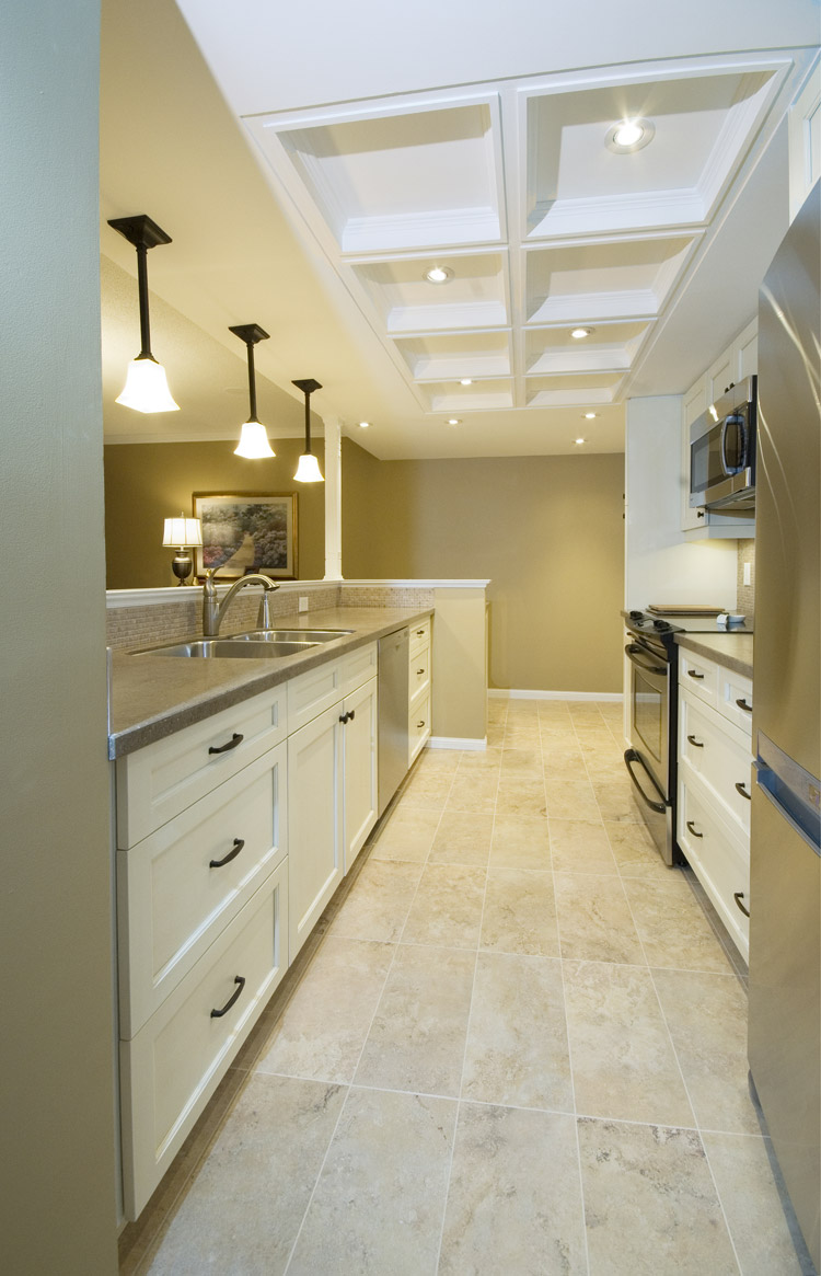 White and grey galley kitchen design featuring white cabinets, stainless steel appliances, tile flooring, and coffered ceiling - Total Living Concepts barrie ontario
