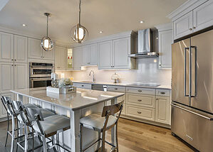 White kitchen design with white cupboards, stainless steel appliances, hardwood floors, and a large island.