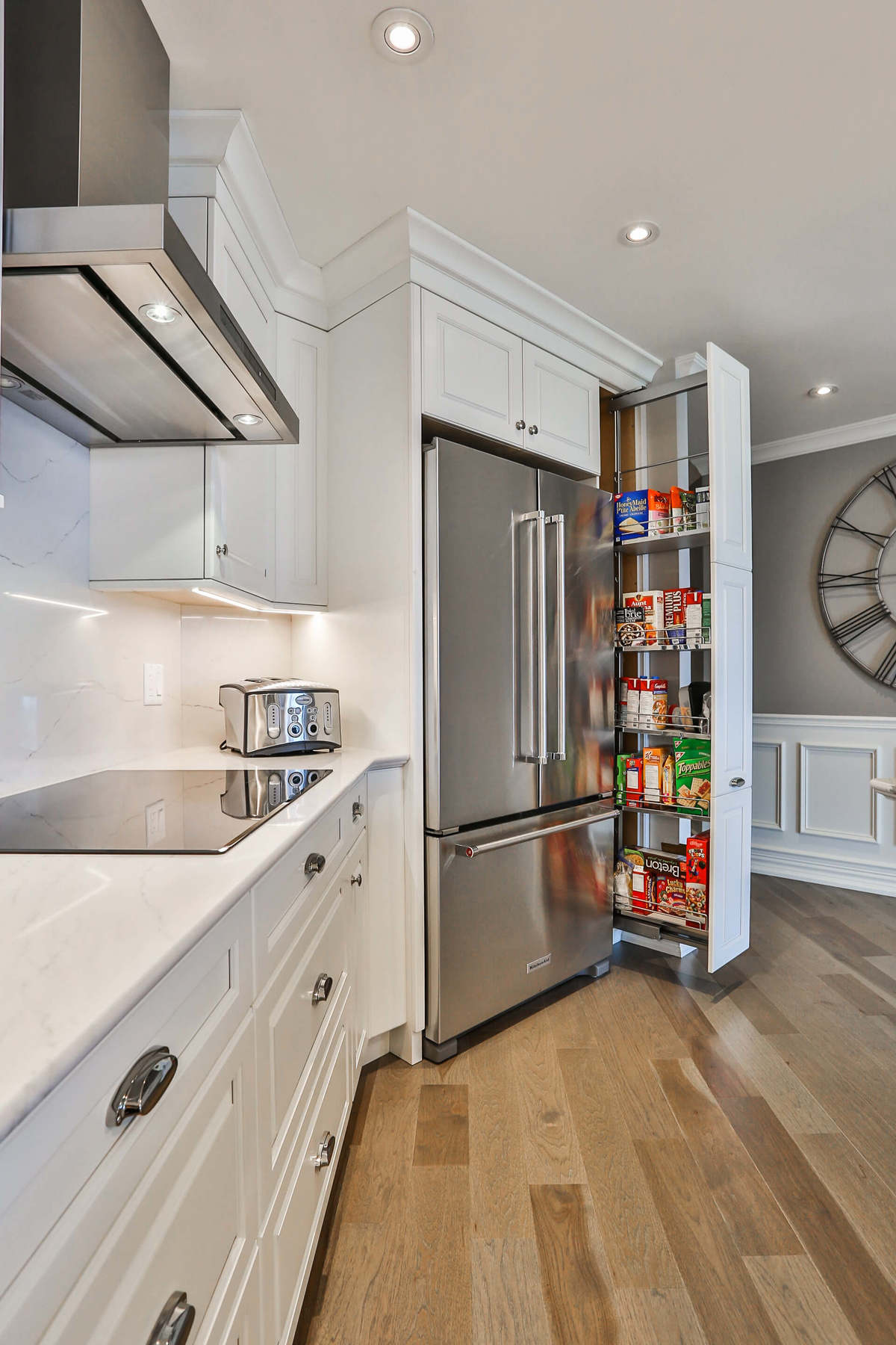 White kitchen design with white cupboards, stainless steel appliances, hardwood floors, and a generous storage.