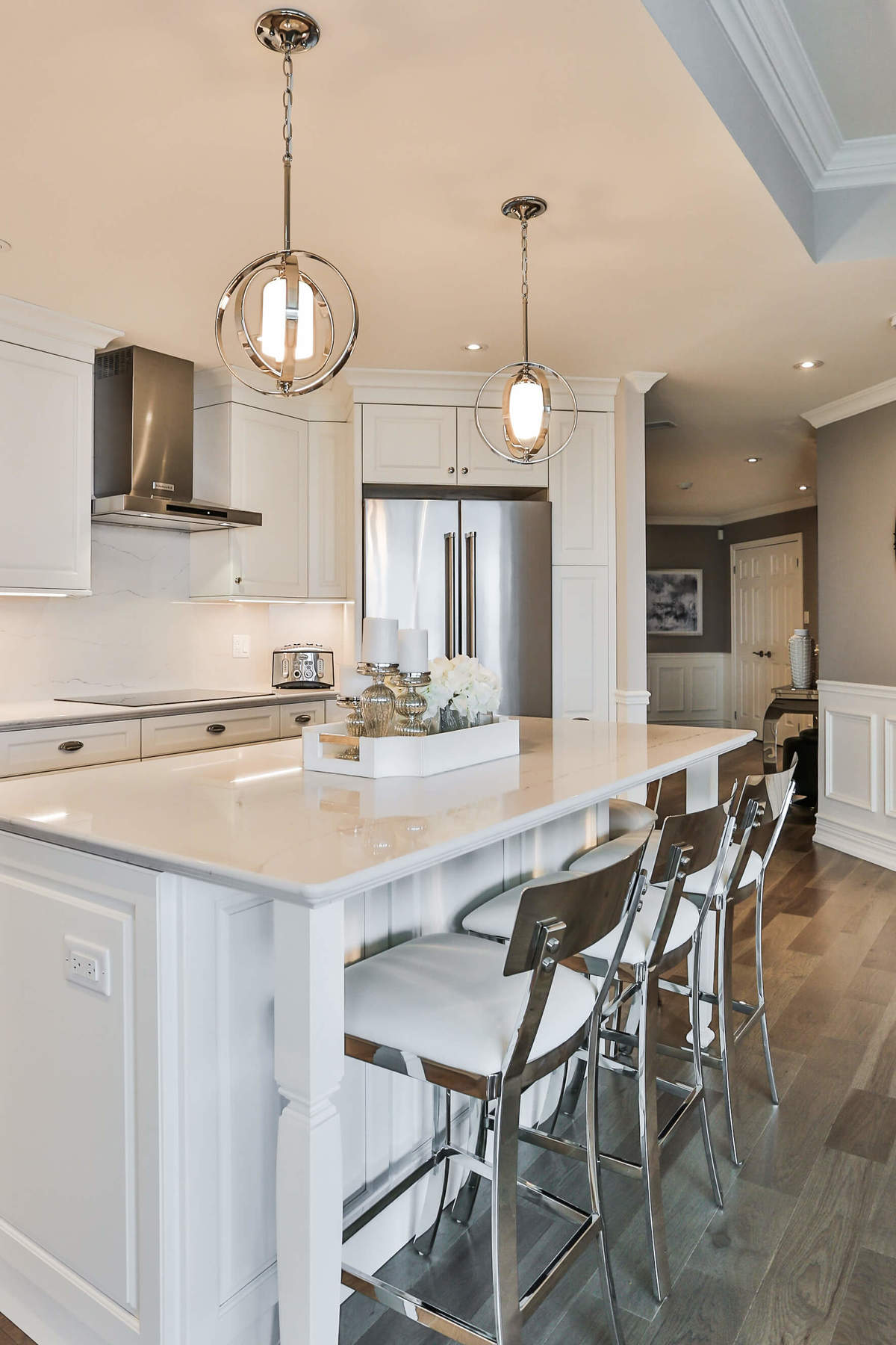 White kitchen design with white cupboards, stainless steel appliances, hardwood floors, and a large island.